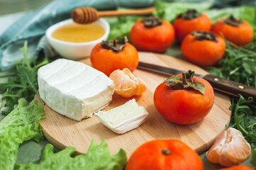 Ingredients and the process of making a vitamin winter salad with persimmons, tangerines and cheese. Selective focus