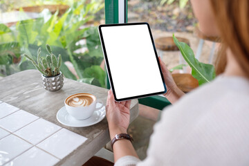 Mockup image of a woman holding digital tablet with blank white desktop screen with coffee cups on...