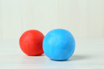 Different color play dough balls on white wooden table, closeup