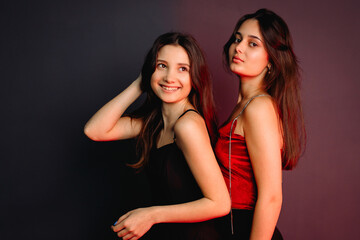 Side view photo of two beautiful self-confident young girls wearing elegant clothes, standing over the two colors background.