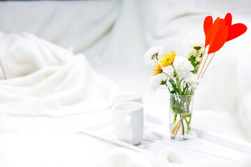 Photo of a romantic breakfast in bed with a cup of tea and vase with flowers over the white background.