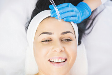 Beautiful woman receiving face cleaning procedure in salon skincare treatment by a professional cosmetologist.