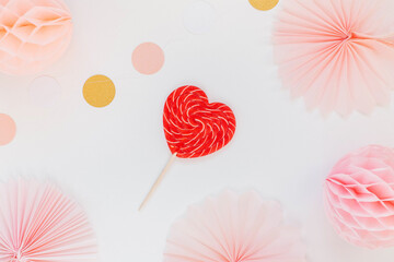 Red heart shaped candy on a pink background with paper decor, paper circles and balls. The concept of love and Valentine's day. Greeting card design for birthday, mother's day