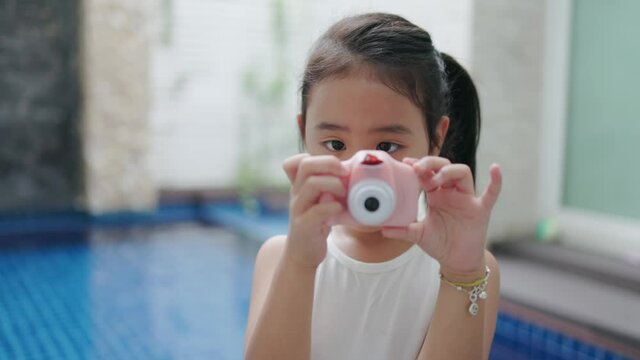 Asian girl taking pictures. Girl holding a pink toy camera taking pictures while smiling wide showing white teeth. Half body camera angle slow-motion