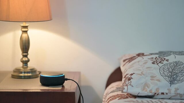 Personal assistant smart speaker on a wooden table with table lamp in a bed room and copy space for Editor's text