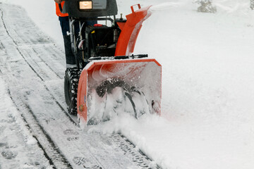 A man works with a snow blower to remove freshly fallen snow from a high voltage transformer driveway.