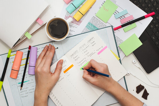 Student's desk. The girl makes notes on stickers in the study schedule. The process of homeschooling or preparing for lectures. Top view of the table with student stationery and notes.