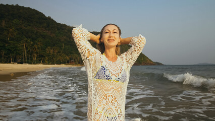 Woman is Wetting her Hair in a White Tunic on the Beach, near the Sea. Blonde in Sunglasses....