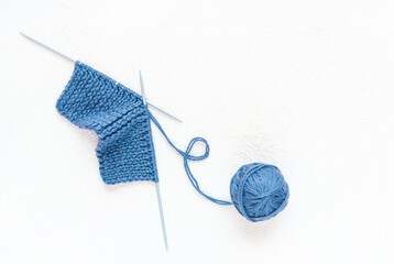 Blue piece of knitting, ball of yarn and a knitting needleson a white concrete background