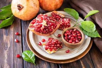 Ripe juicy pomegranate fruits in a wooden bowl on a rustic table. Diet and healthy food.