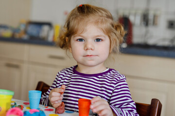 Adorable cute little toddler girl with colorful clay. Healthy baby playing and creating toys from play dough. Small kid molding modeling clay and learning