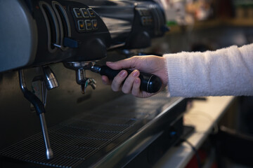 A female hand holds a holder in a professional coffee machine.