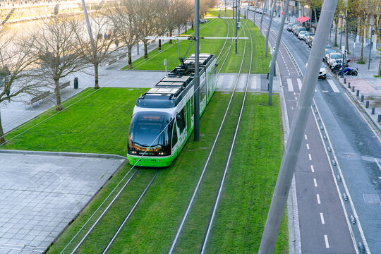 BILBAO, SPAIN-DECEMBER 18, 2021 : Euskotren city tram runs on tramway track. Modern transport in Europe. Smart city. Above view of city ram near the river. Electric vehicle. Green transport.