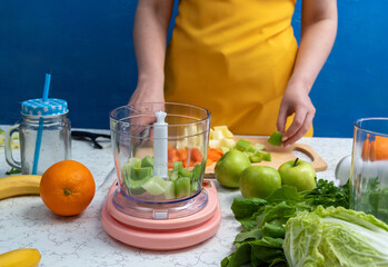 Pieces of celery in blender bowl, which stands on scales. There are other ingredients on table nearby. The process of making smoothies. Selective focus.