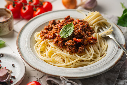 Pasta spaghetti bolognese with minced beef sauce, tomatoes, parmesan cheese and fresh basil in a plate on white tile background. Italian food