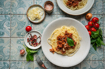 Pasta spaghetti bolognese with minced beef sauce, tomatoes, parmesan cheese and fresh basil in a plate on tile background. Italian food, top view
