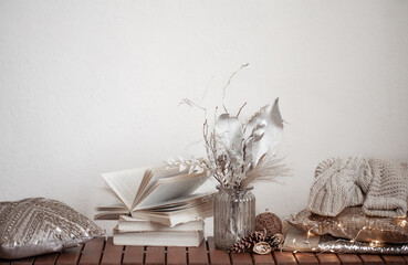 Cozy background with books, a vase of dried flowers and decorative cushes.
