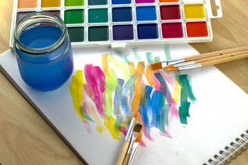 watercolor paints a jar of water and brushes on a white sheet with flower samples