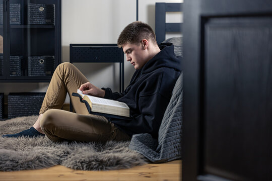 A young man sits in a room and reads the Bible.