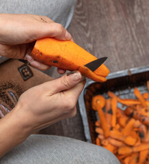 A woman peels a carrot with a knife.