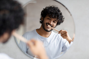 Toothcare routine concept. Young indian guy cleaning teeth in the morning using toothbrush and...