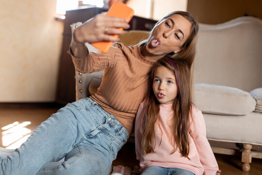 Portrait of smiling mom and daughter taking selfie using smartphone