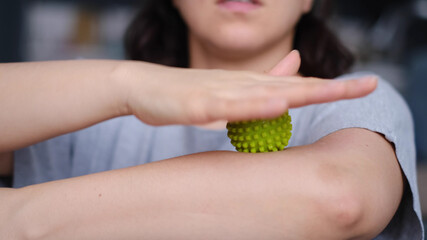 Close-up a young woman is working out the arm muscles with a green myofascial ball. Woman doing...