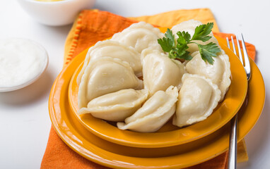 Dumplings (vareniki, pierogi, pyrohy) with potatoes in ceramic bowl on white