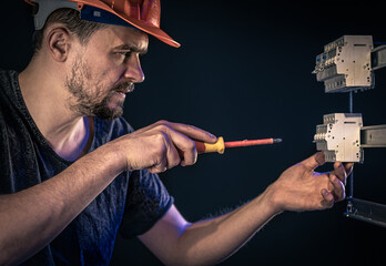 A male electrician works in a switchboard with an electrical connecting cable.