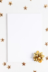 Greeting card mockup on a white wooden table with golden confetti in the form of stars top view. Empty template with copy space.