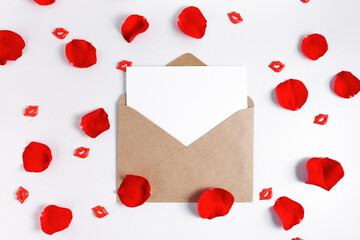 Greeting card mockup in an open envelope on a white wooden table with rose petals. Empty template for design with copy space.