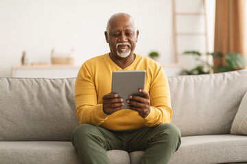 Senior African American Male Using Digital Tablet Reading Online Indoor