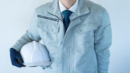 作業服にネクタイの男性。ヘルメットを抱える。建設業イメージ。