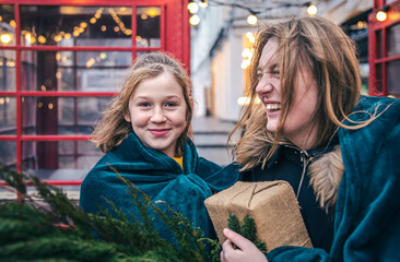 A little girl and young woman with thuja branches and a gift under a plaid.