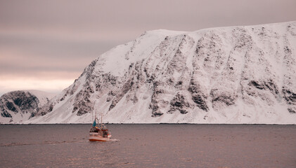 Cod fishing boats at sunset in Norwegian fjords with snowy mountains