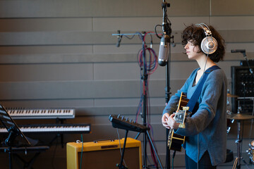 A young singer woman recording a song in a real messy studio with her guitar
