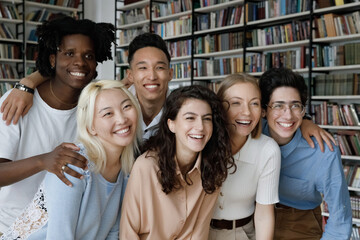 Diverse group of cheerful happy student girls and guys posing in library, looking at camera away,...