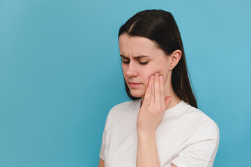 Close up of young brunette female suffering from toothache, isolated on blue studio background....