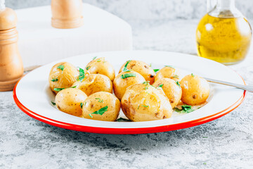 Fresh boiled baby potatoes with fresh dill on a white plate. Stone background.