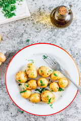 Fresh boiled baby potatoes with fresh dill on a white plate. Stone background.