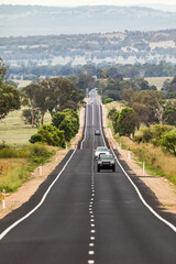 Cars travelling along a very long, straight single lane paved highway in rural New South Wales, Australia.