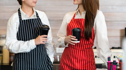 Couple Asian woman wearing an apron, holding a coffee cup and stands behind the counter in a coffee shop. Young lesbian couple runs a cafe together