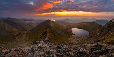 Beautiful vibrant sunrise overlooking Red Tarn and Ullswater from the summit of Helvellyn mountain...