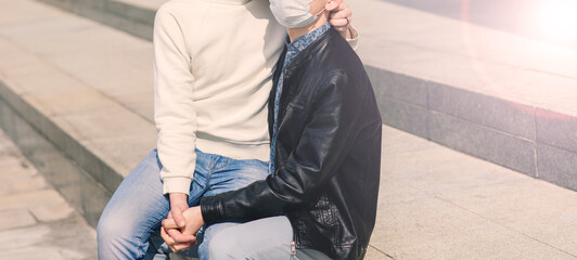 Young gay couple wearing medical mask, hugging and kissing at the city.