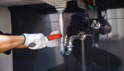 Plumber fixing white sink pipe with adjustable wrench.