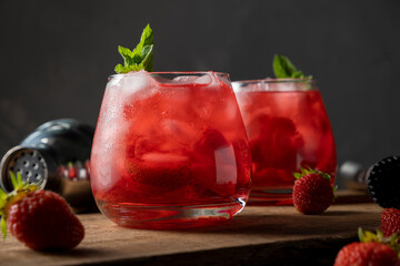 Red drink with strawberry, ice and mint. Refreshing summer cocktail in a glass on wooden table