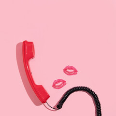 Valentines day creative layout with bright red retro phone handset and kiss prints on pastel pink...
