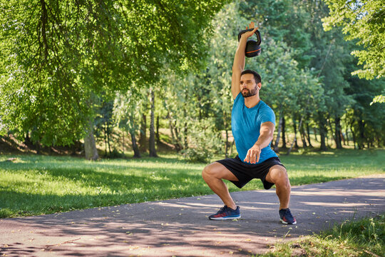 Athletic man does squats with kettlebell in park