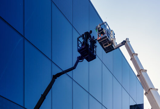 Cleaner worker using a cherry picker to clean a glas  facade of a contemporary office building. 