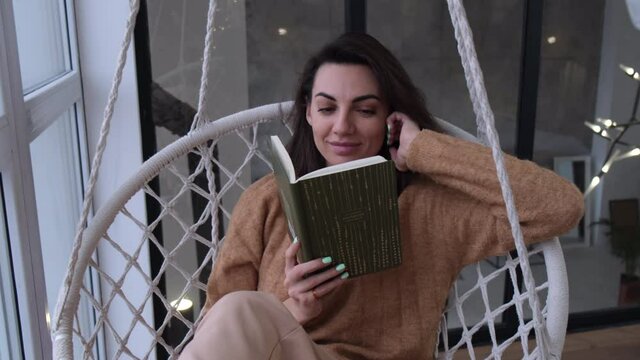 A young woman at home in an egg chair sits with a notebook, a diary and rereads plans and goals for the year with a smile 